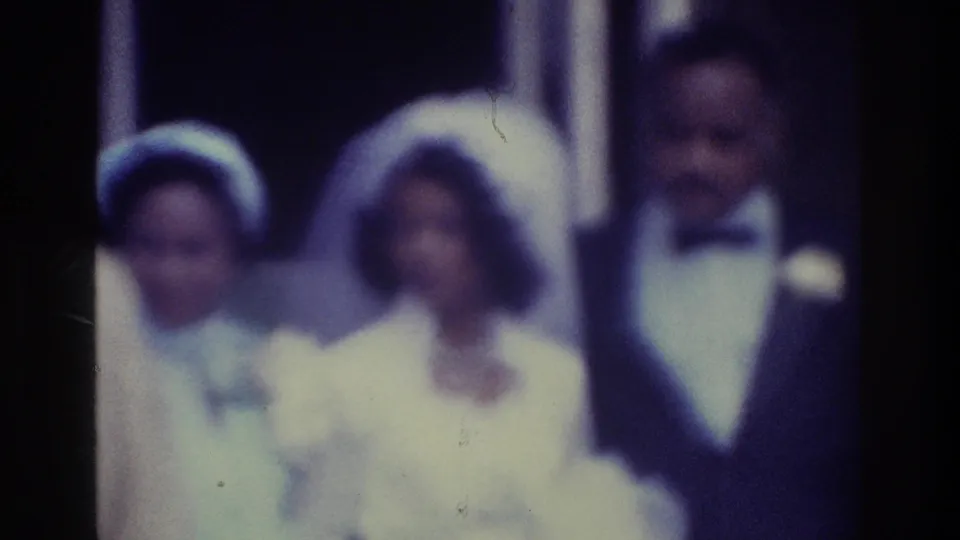 Color-faded 1975 Bronx wedding frame with bride, groom, and guests grouped near an entrance, all rendered in soft focus.
