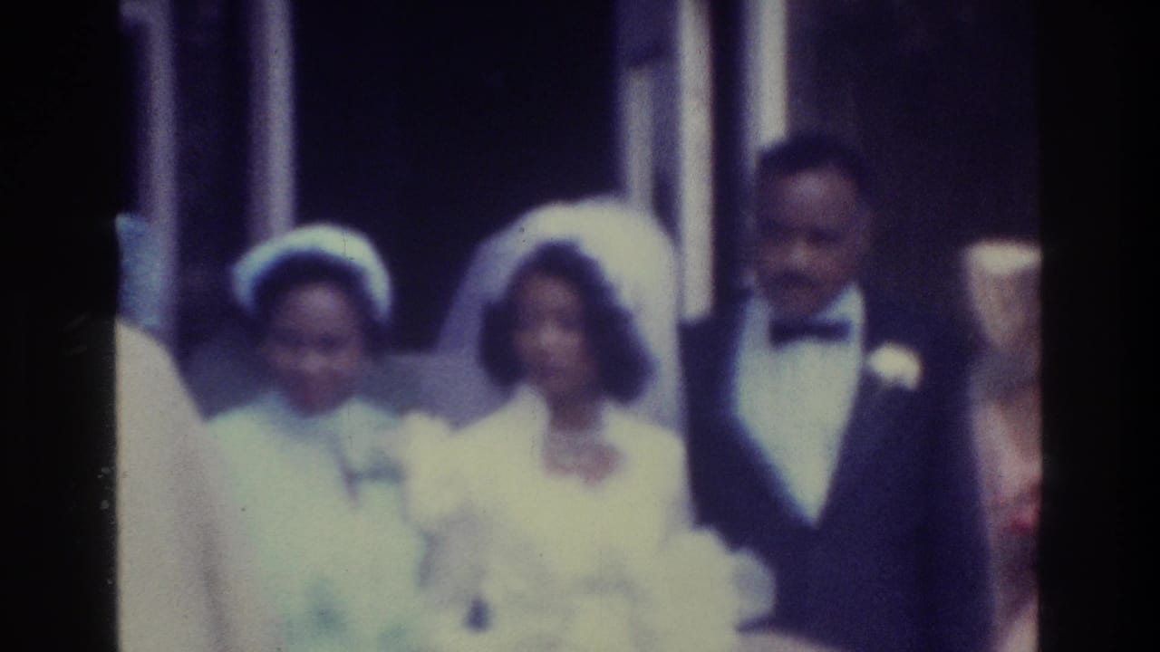 1975 Bronx home-movie frame showing a Black bride in a white veil beside the groom in a tuxedo, with guests nearby.