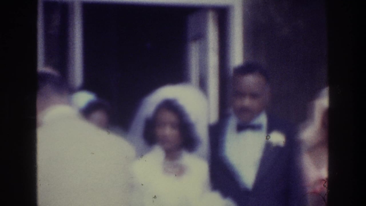 Bride and groom appear beside guests as a person in light clothing crosses foreground.