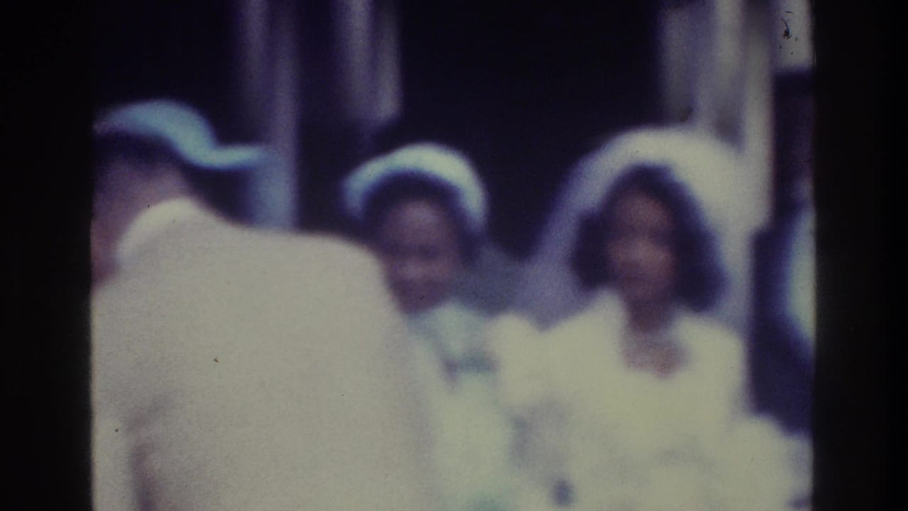 Soft 1975 Bronx 8mm frame showing a groom near formally dressed women, with faces and clothing blurred by focus and exposure.