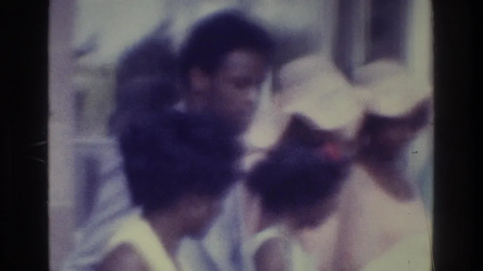 Soft 8mm wedding frame from the Bronx showing formally dressed guests around a woman with a red ribbon and others in hats.