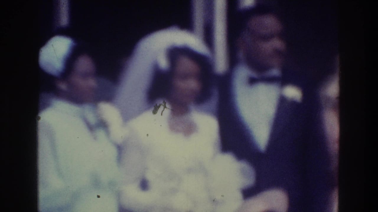 The bride and groom appear framed by guests in light formal clothing, including a woman in a pale hat, in the supplied Bronx wedding home-movie scene.