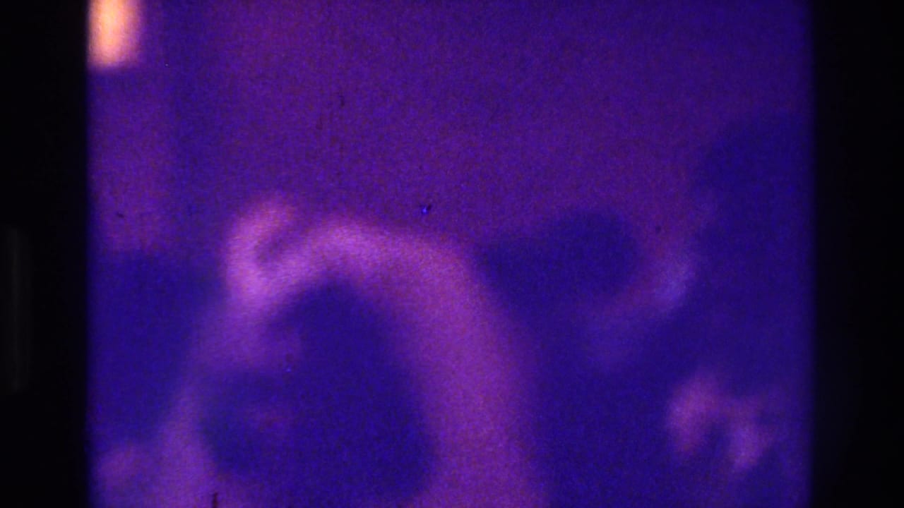 Soft 8mm 1975 Bronx wedding frame with indistinct figures in a dim church interior and strong purple-blue fading.