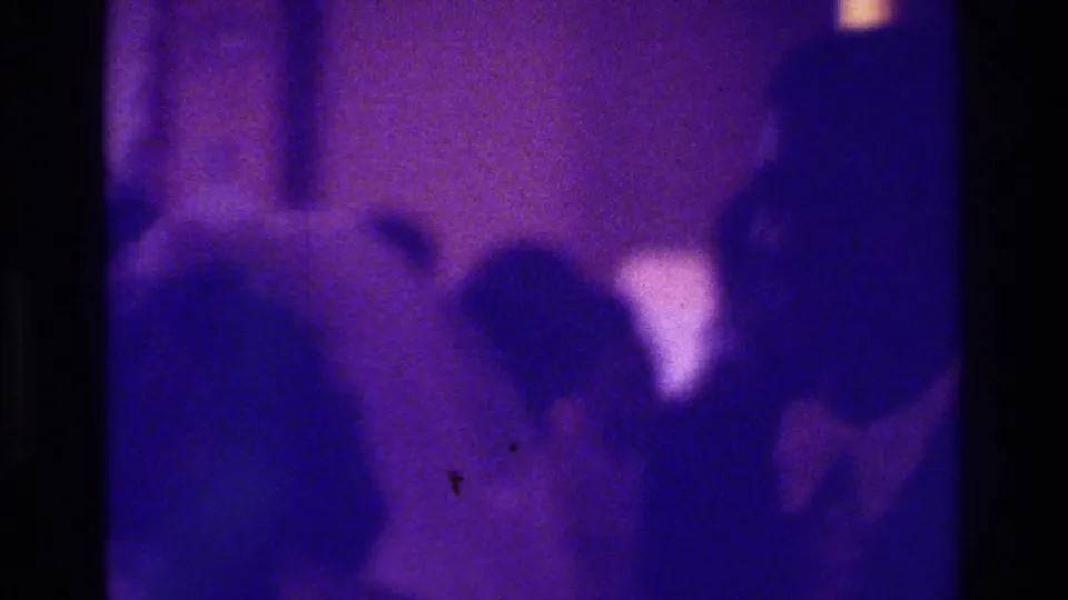 Multiple wedding-party silhouettes stand or move near a pale bridal figure in this grainy 1975 Bronx 8mm frame.