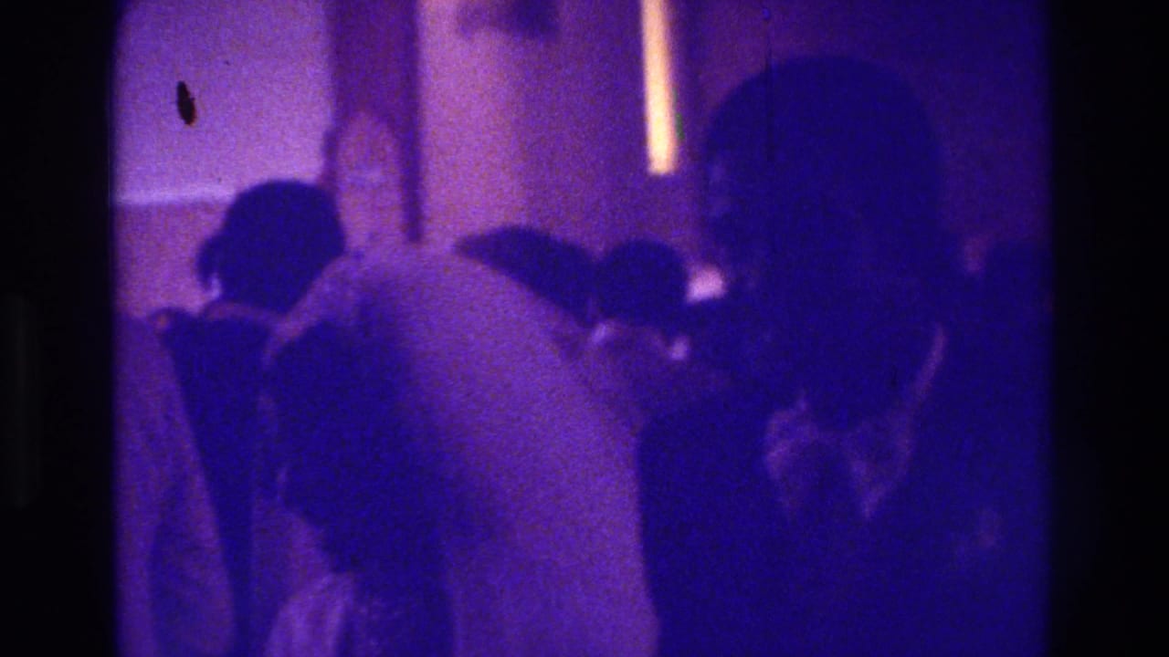 Bride in white seen from behind with seated guests in a dim interior.