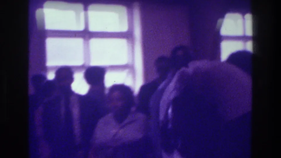 Congregants stand and face different directions inside a Bronx church, with bright windows and a heavy purple 8mm cast.