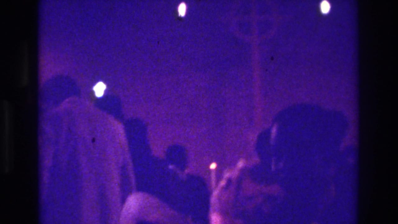 1975 Bronx 8mm frame showing worshippers in a dark church interior lit by small candle flames and purple-blue exposure.