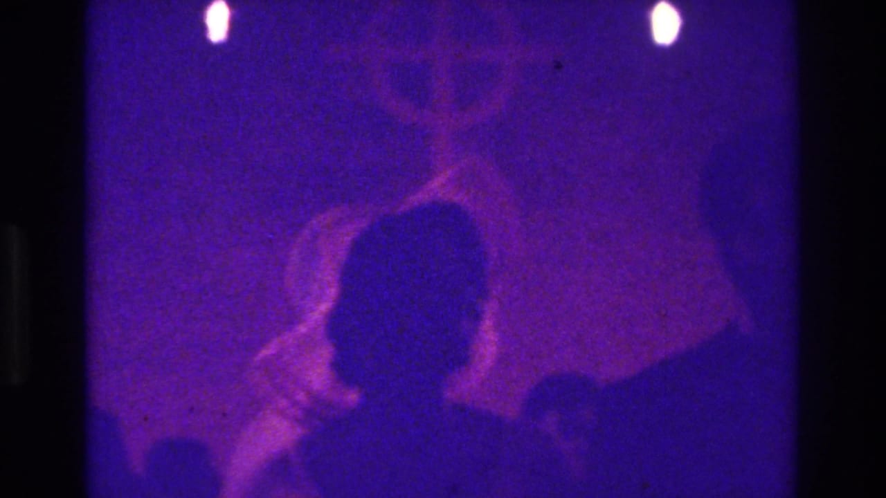 Backlit attendee silhouettes with purple light and a faint cross-like shape.