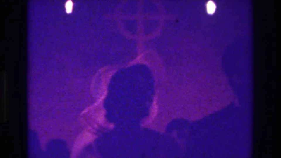 1975 Bronx home-movie frame showing backlit figures in a purple-lit religious or ceremonial space with a faint cross-like form.