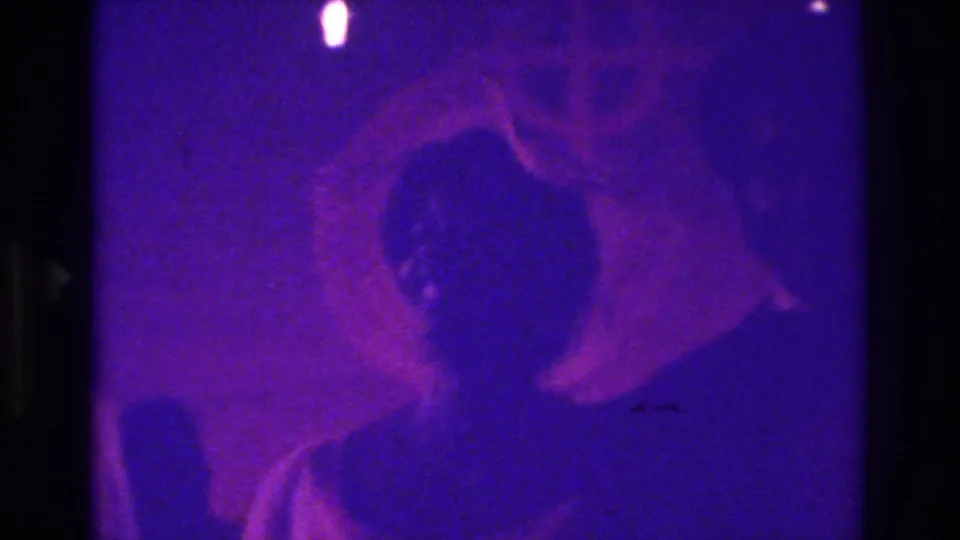 1975 Bronx 8mm frame with close, dark attendee silhouettes, purple illumination, soft grain, and visible film handling artifacts.