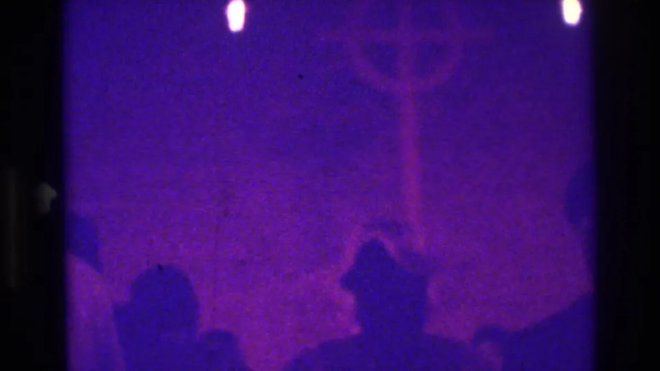 1975 Bronx 8mm still showing a grainy purple interior, a cross-like shape, and two shadowed figures at the bottom of the frame.