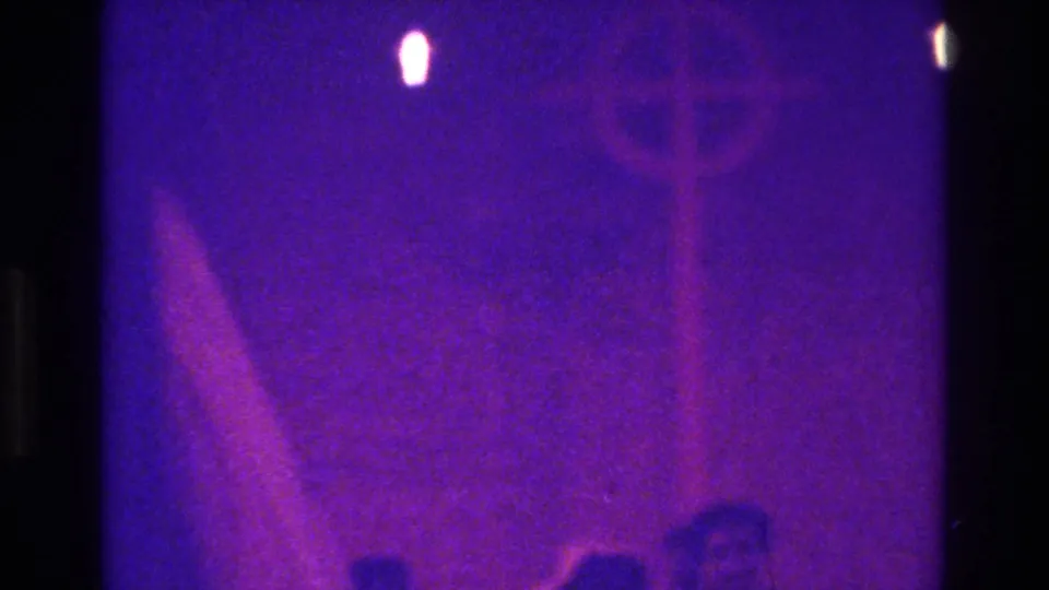 The 8mm frame shows a hazy purple view of church guests during a Bronx wedding, with aisle figures mostly reduced to silhouettes.