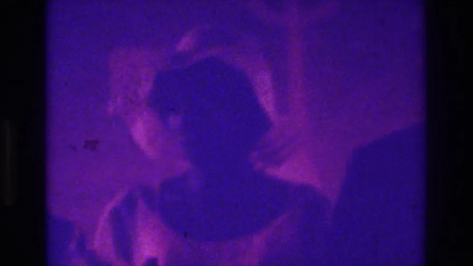 Close, grainy 1975 Bronx home-movie frame with wedding guests in the foreground and a crowded church scene behind them.