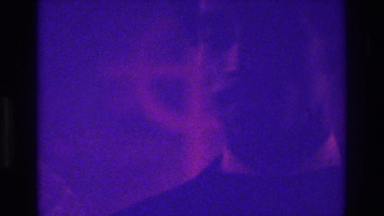 Faint suited figure in a purple-tinted, grainy 8mm frame.
