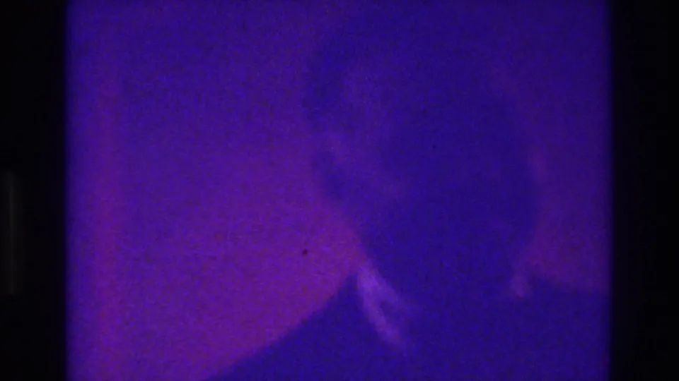 A close, indistinct suited figure appears in the lower portion of a purple-shifted 1975 Bronx home-movie frame.