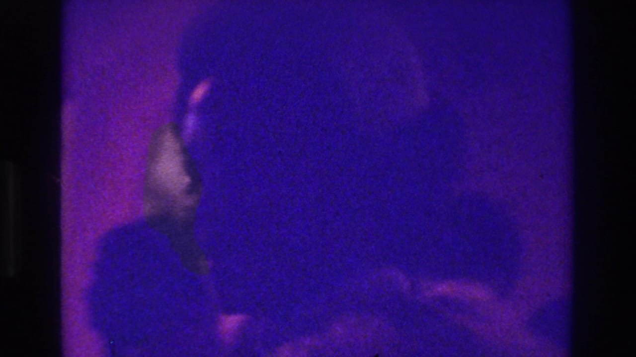 1975 Bronx 8mm frame with an indistinct person at left, mostly obscured by purple-blue low light, grain, and motion blur.