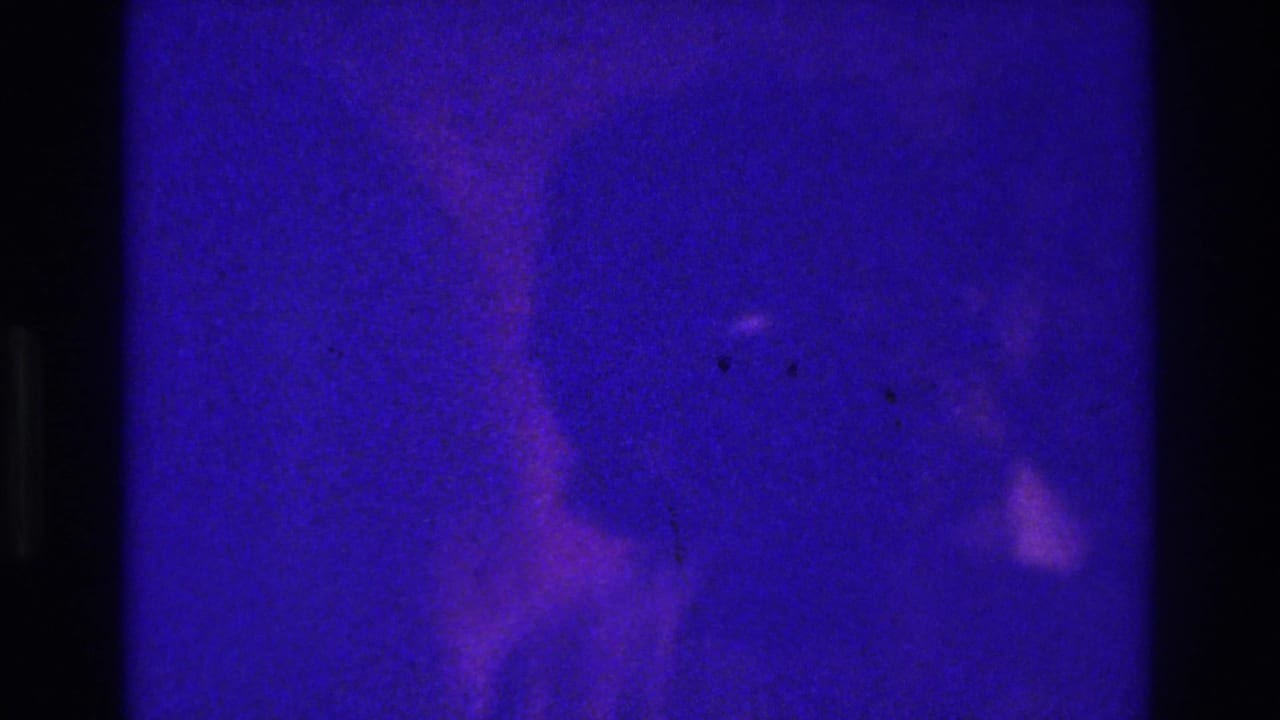 1975 Bronx 8mm home-movie frame with heavy blue-purple cast, dark gate edges, and a barely visible person-like silhouette.