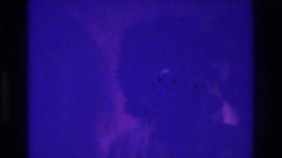 1975 Bronx 8mm home-movie frame with heavy blue-purple cast, dark gate edges, and a barely visible person-like silhouette.