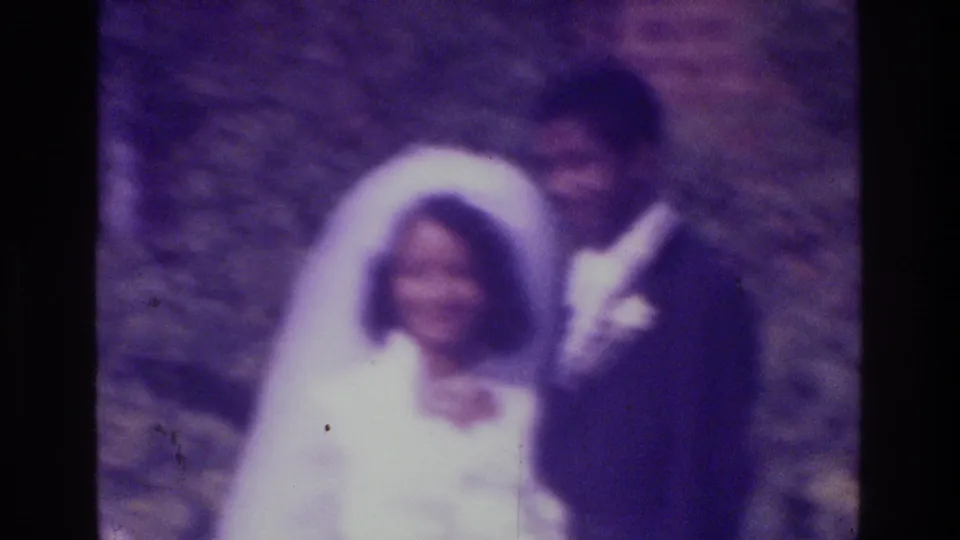 1975 Bronx wedding footage shows a smiling bride in veil with the groom beside her against a soft outdoor background.