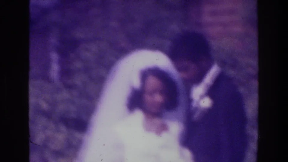 1975 Bronx home-movie wedding frame shows the groom looking toward the bride during a quiet outdoor portrait pose.