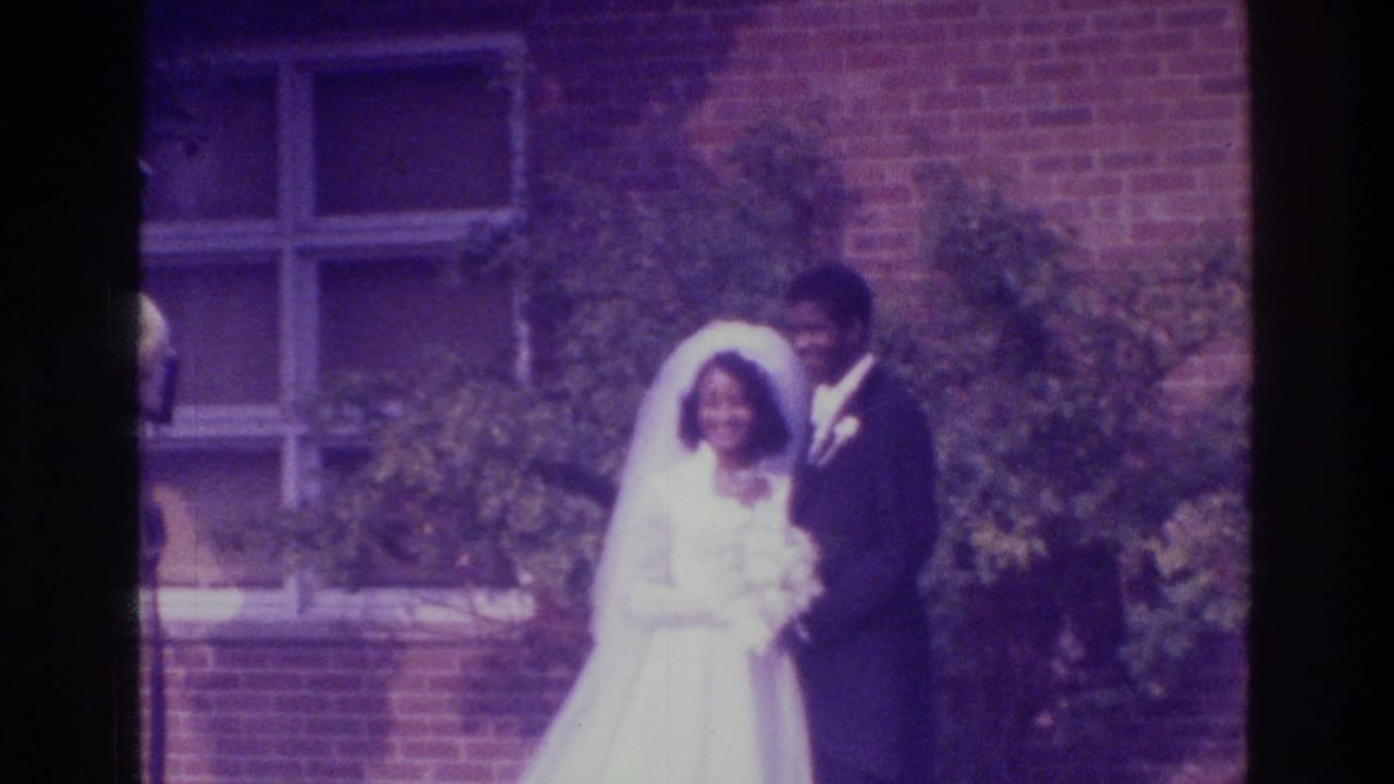 Bride and groom smiling while posed near a window and shrubs.