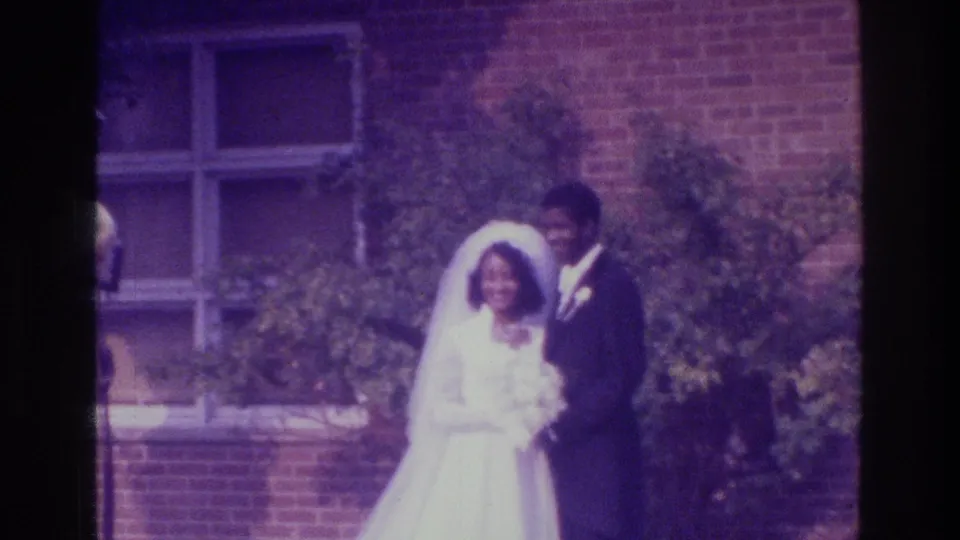 1975 Bronx wedding frame with the bride holding a bouquet as the groom stands beside her before a brick building.