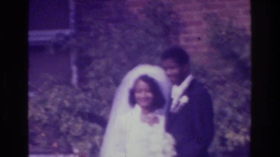 1975 Bronx home-movie still of a bride and groom smiling outdoors, with soft focus and purple film cast.