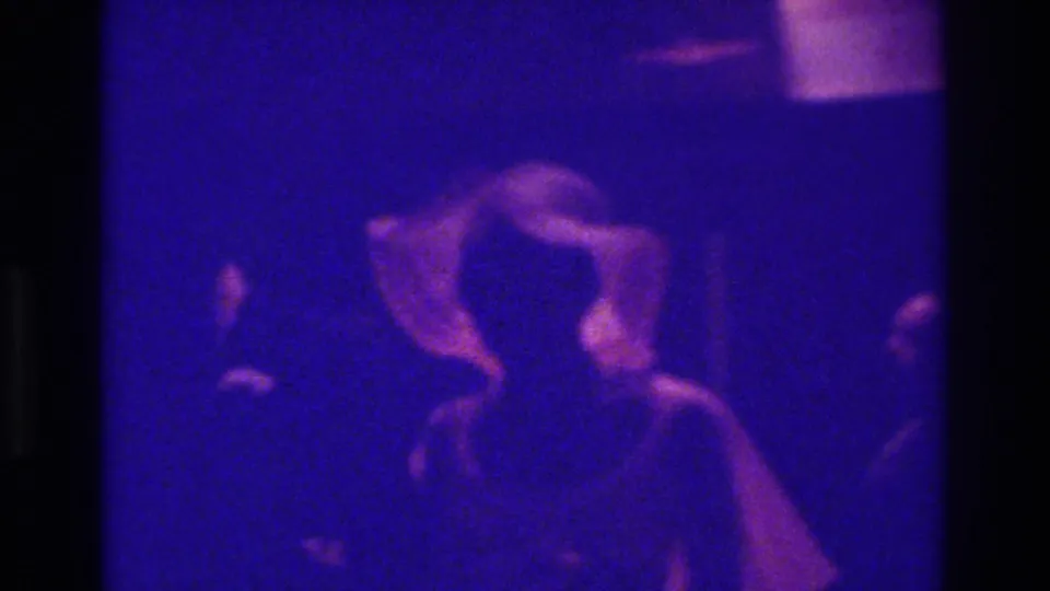 1975 Bronx wedding footage appears to show a bride-like figure in a large white hat or veil among guests in a dim interior.