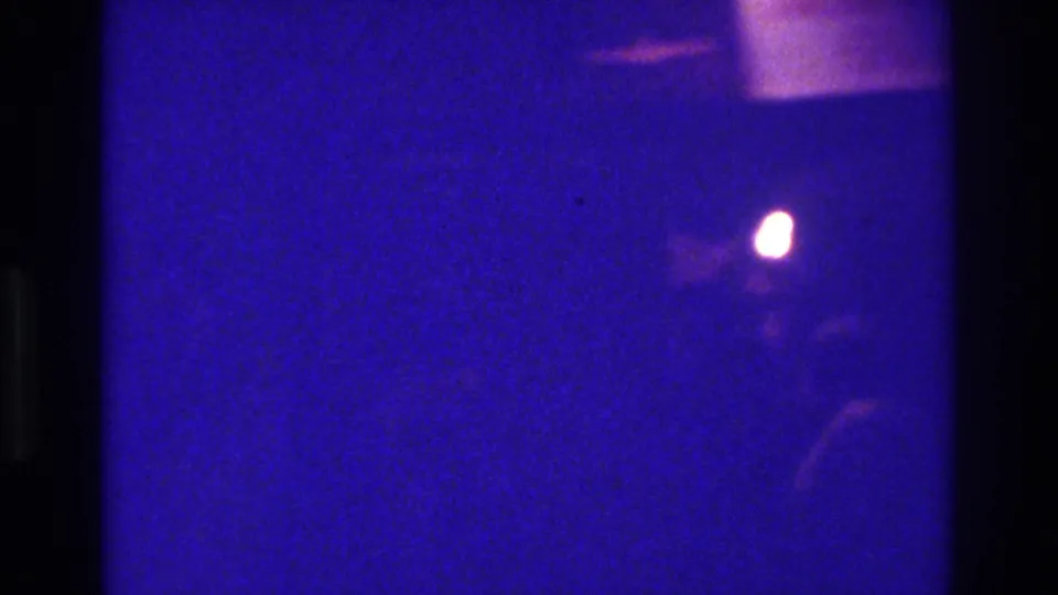 The final 1975 Bronx 8mm frame is mostly dark, with one small glowing light and faint silhouettes in the wedding interior.