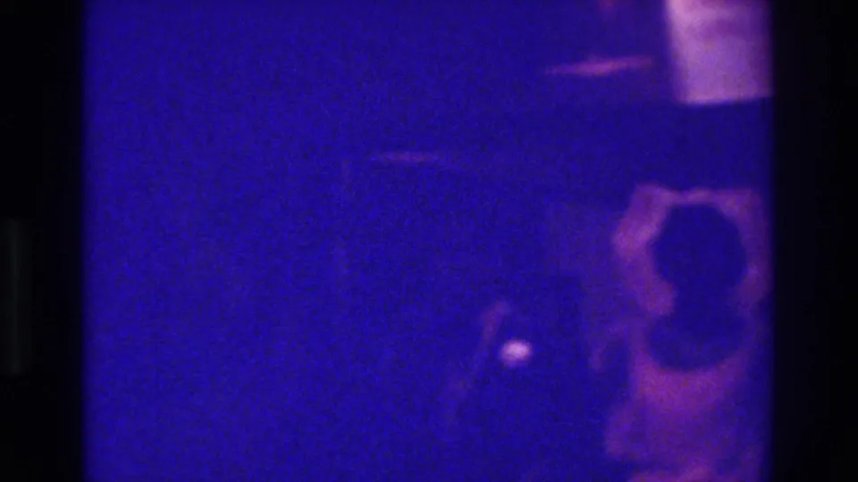 Blue-tinted 1975 Bronx home-movie frame showing a dim human figure or couple-like shape near the right edge.