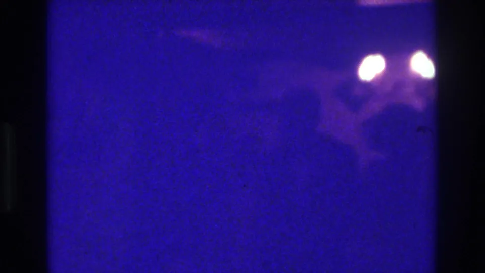 1975 Bronx 8mm frame with two glowing lights and a shadowed person-like form in blue-purple darkness.