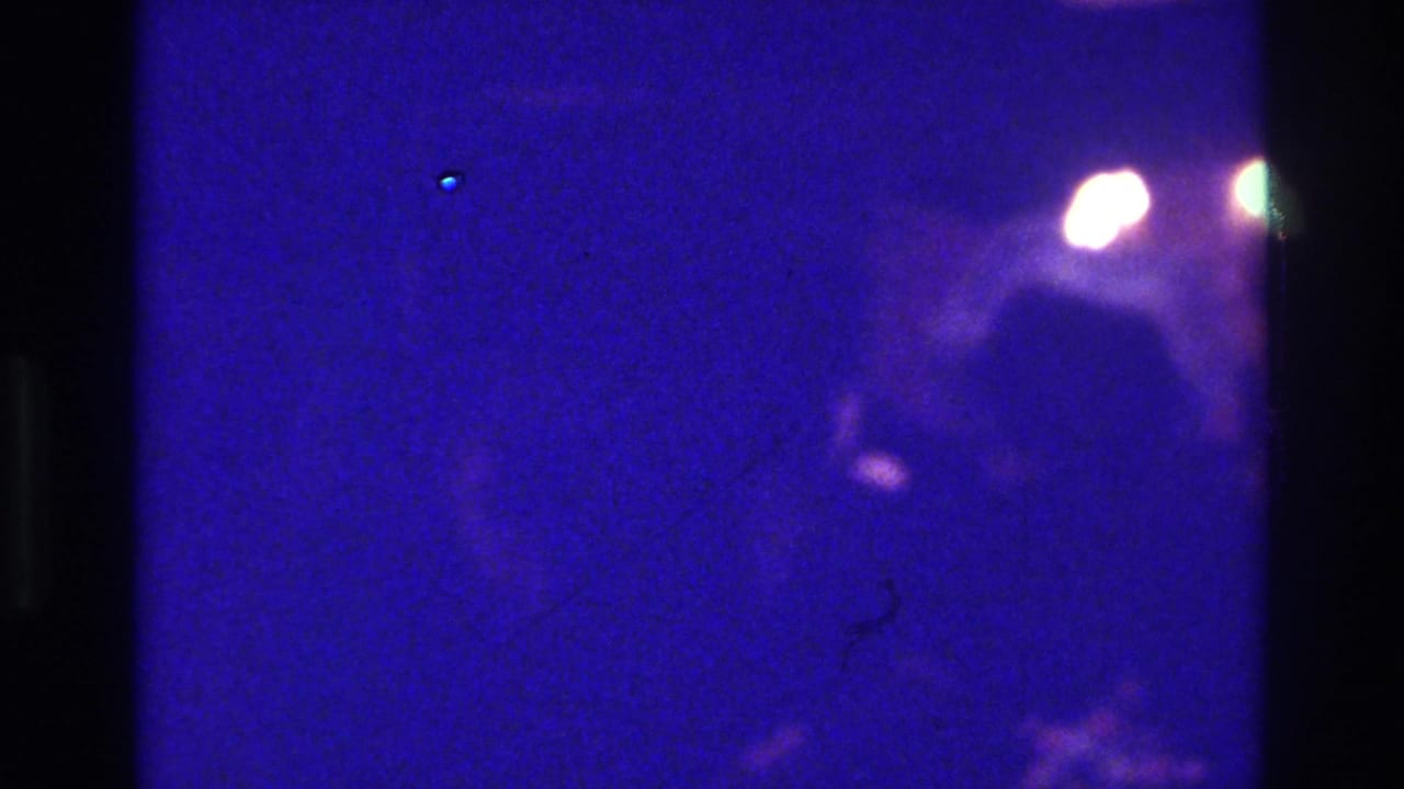 1975 Bronx 8mm frame with a dark purple-blue field, black film-edge bands, small light flares, and little identifiable detail.
