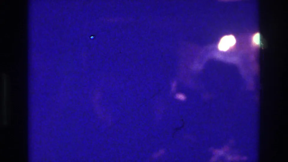 1975 Bronx 8mm frame with a dark purple-blue field, black film-edge bands, small light flares, and little identifiable detail.