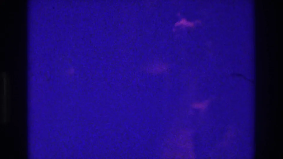 1975 Bronx 8mm frame with scattered pinkish light marks, deep purple-blue color shift, underexposure, and analog grain.