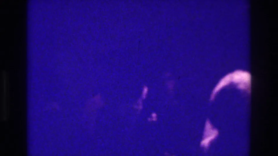 The bride's veil remains visible at the right edge of this 1975 Bronx wedding home movie frame, surrounded by dark guests and heavy grain.