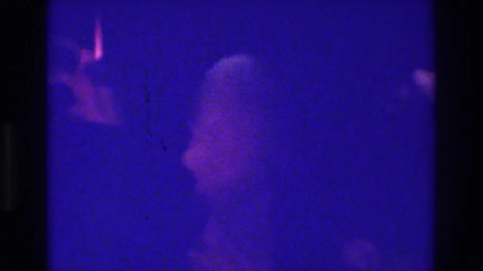 1975 Bronx 8mm frame showing a blurred person-like pale form in deep blue light, with visible grain, scratches, and gate borders.
