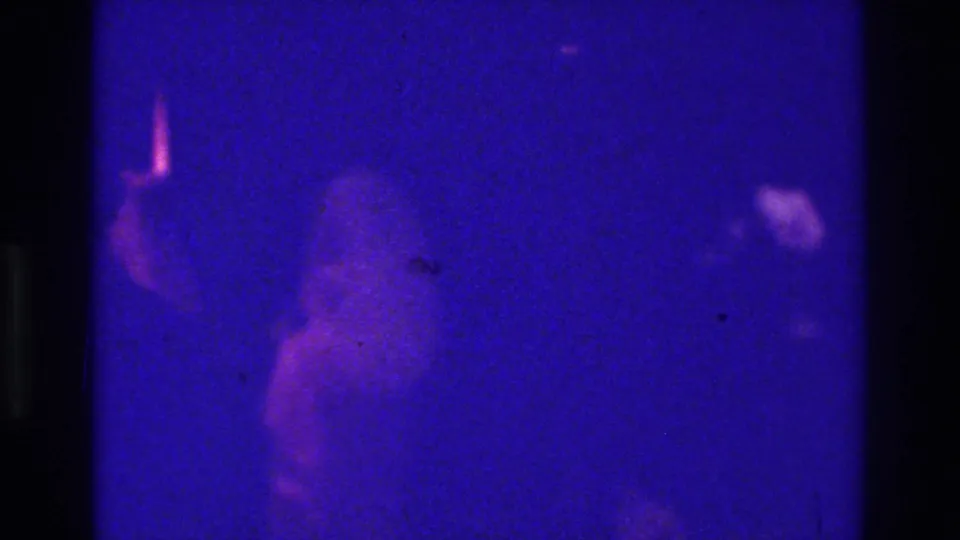 1975 Bronx 8mm frame with a faint figure-like shape in blue light, surrounded by heavy grain, scratches, and dark frame borders.