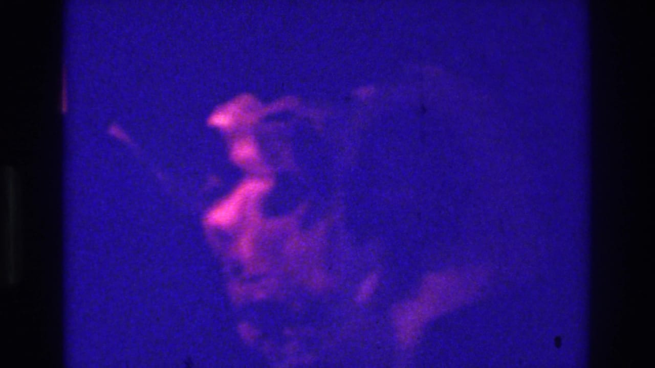 Blurred human figure in magenta light against a dark blue interior.