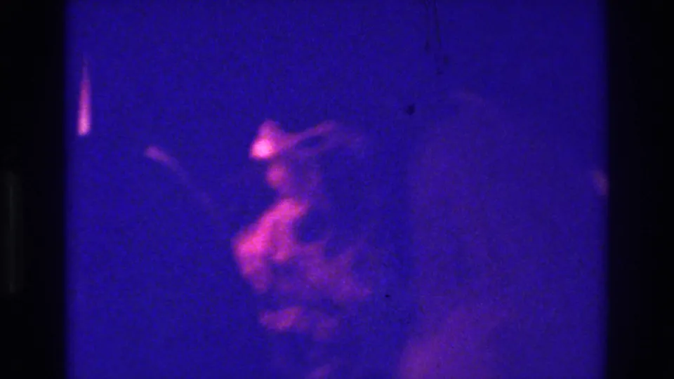 1975 Bronx home-movie frame showing a low-lit pub scene with a blurred person near the lower left and heavy blue cast.
