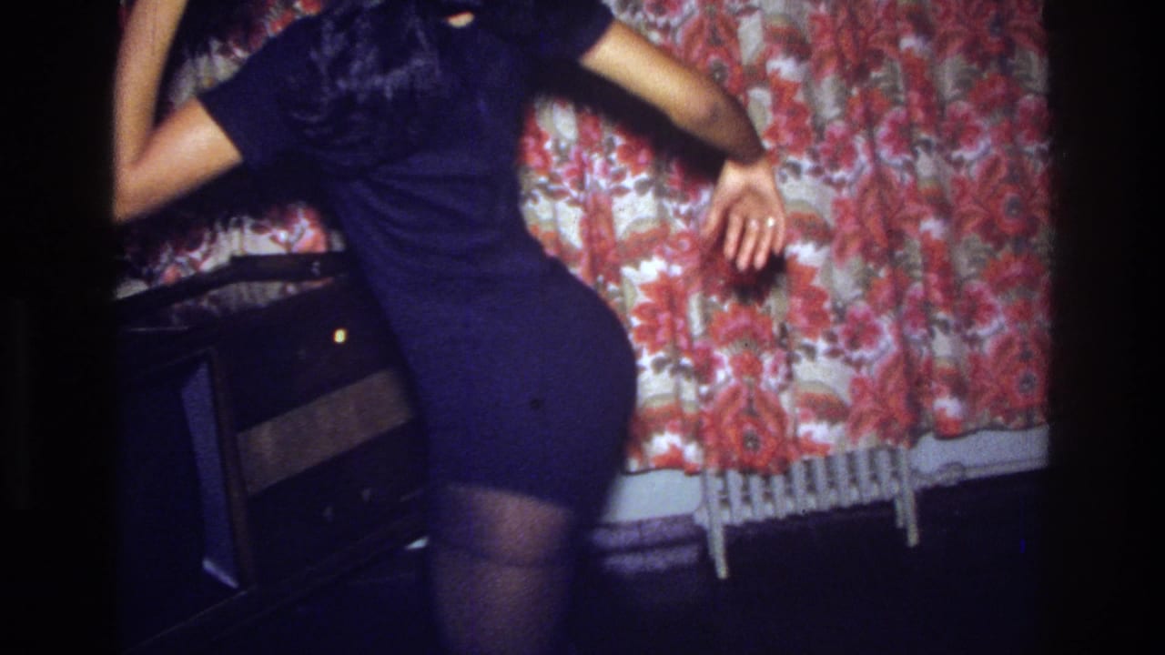 A 1975 Bronx home-movie frame shows the woman dancing in profile near a floral curtain, with a radiator partly visible below.