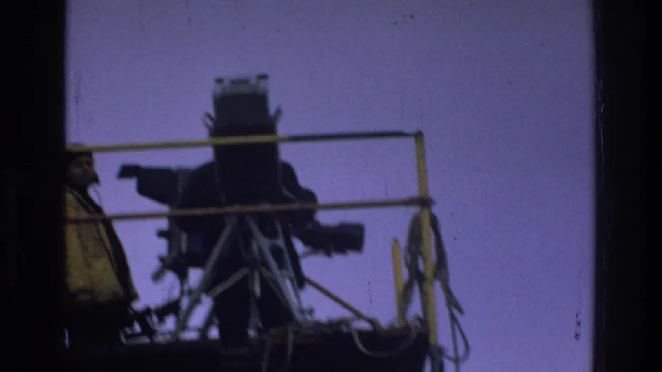 A crew member in a yellow jacket stands near a large silhouetted camera on the raised platform in the 1975 Bronx footage.