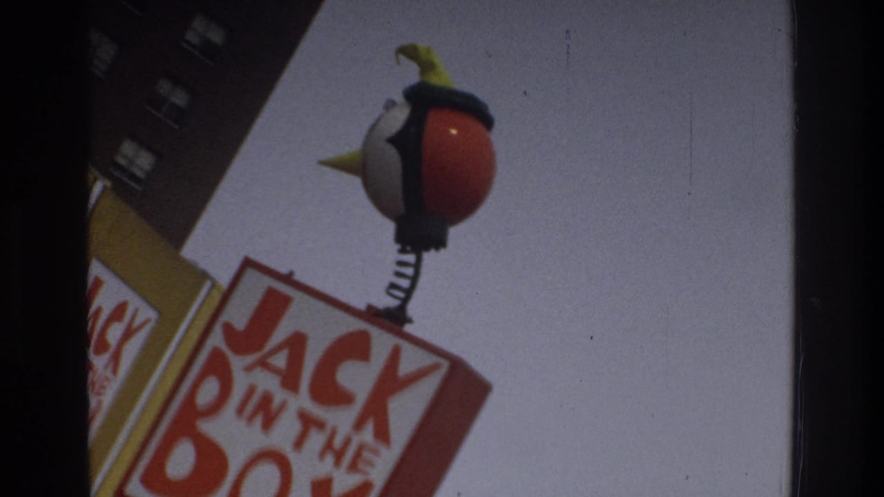 1975 Bronx 8mm frame showing a Jack in the Box sign topped by a round mascot figure on a spring, framed from below beside a brick building.