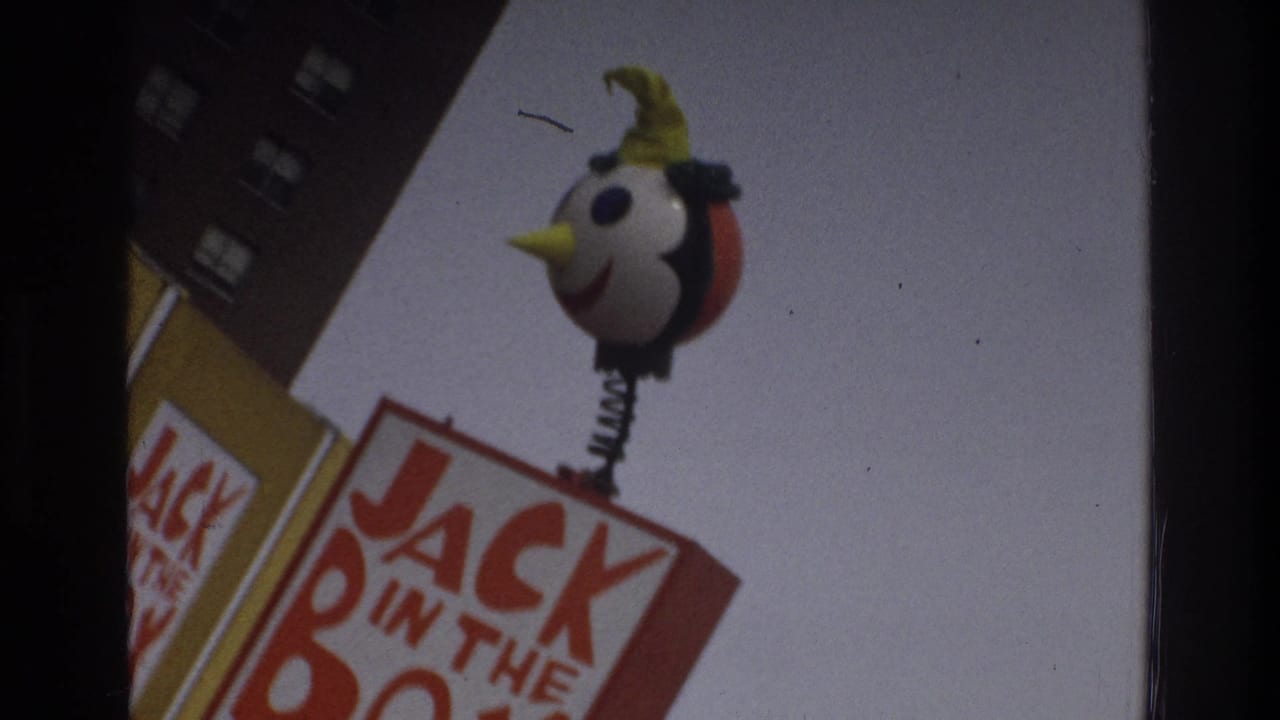 Smiling mascot figure above a Jack in the Box sign beside a brick building.