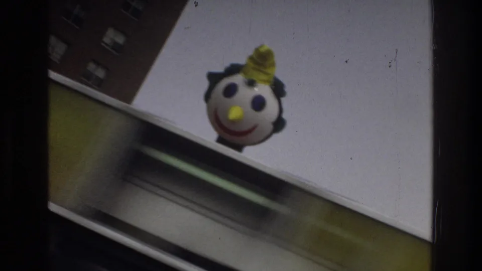 1975 Bronx 8mm frame showing the round Jack in the Box mascot head near the top of a storefront or sign edge, with partial sign lettering and sky visible.