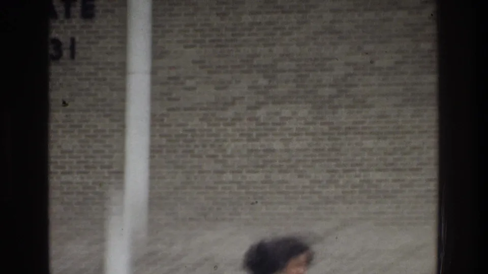 The 8mm frame looks across the school wall and vertical window bars, with a blurred passerby or partial figure near the bottom edge.