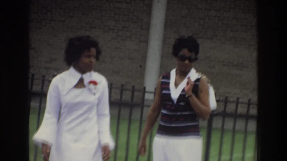 In a 1975 Bronx street scene, two Black women walk together, one in a white dress and one in a striped top and white skirt.