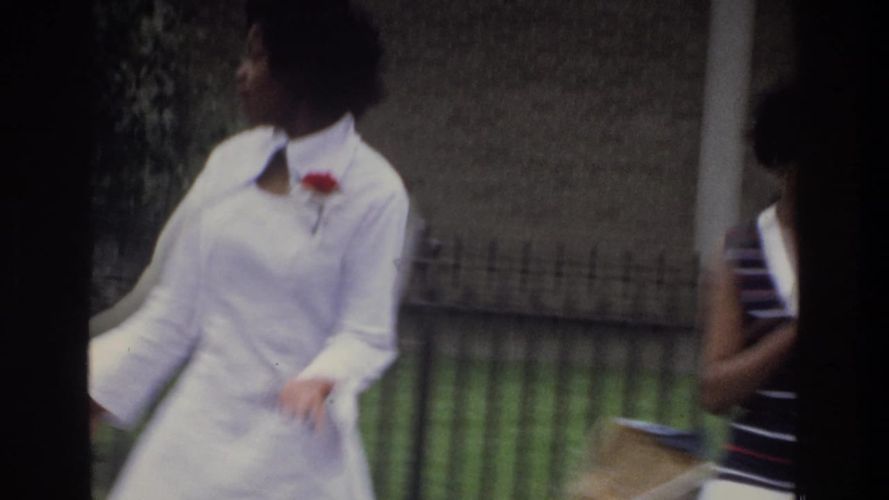 Close view of two women mid-stride outdoors; woman in white dress with red corsage dominates frame, woman in striped top visible at right edge; natural motion blur present.