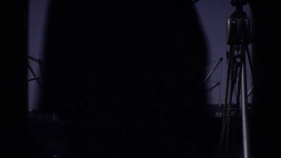 Heavily shadowed opening frame from a 1975 New York dock, showing rope or cable rigging and a partial crane arm through a near-opaque foreground silhouette.