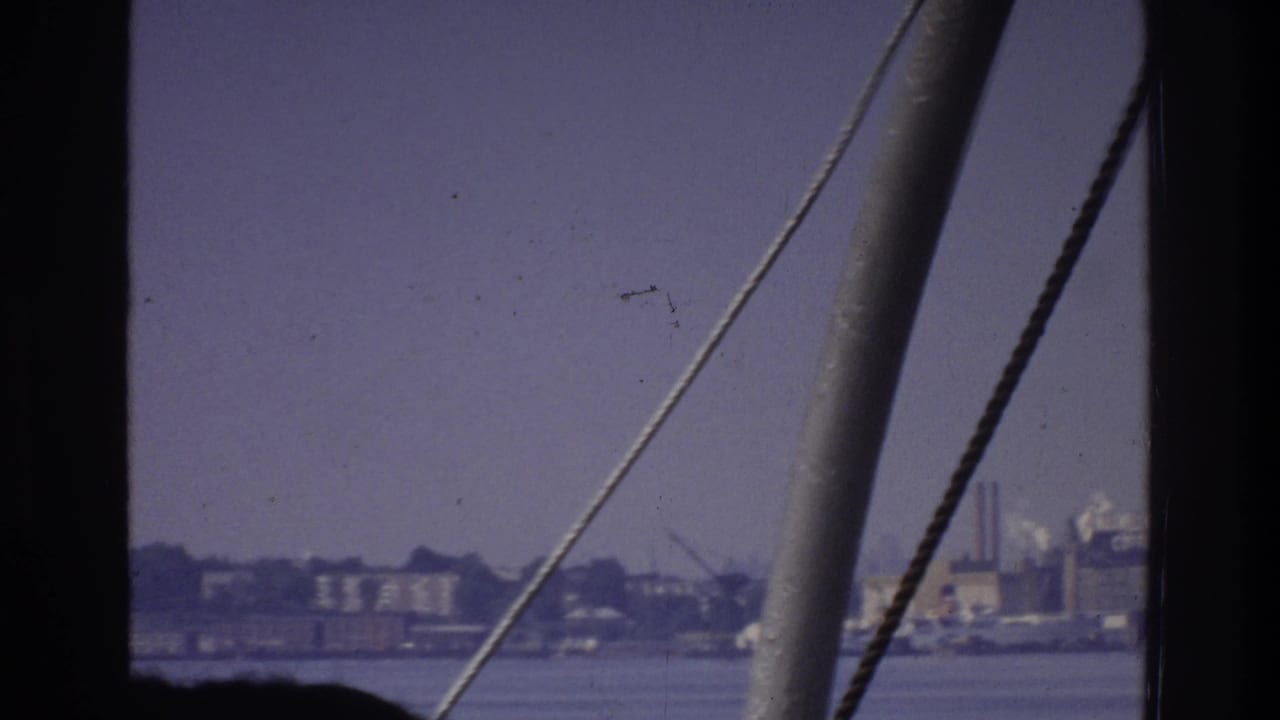 8mm home movie footage circa 1975 from a vessel, showing boat rigging in the foreground and a low industrial waterfront — possibly the Bronx — across calm water.