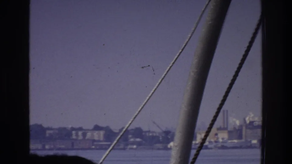 8mm home movie footage circa 1975 from a vessel, showing boat rigging in the foreground and a low industrial waterfront — possibly the Bronx — across calm water.